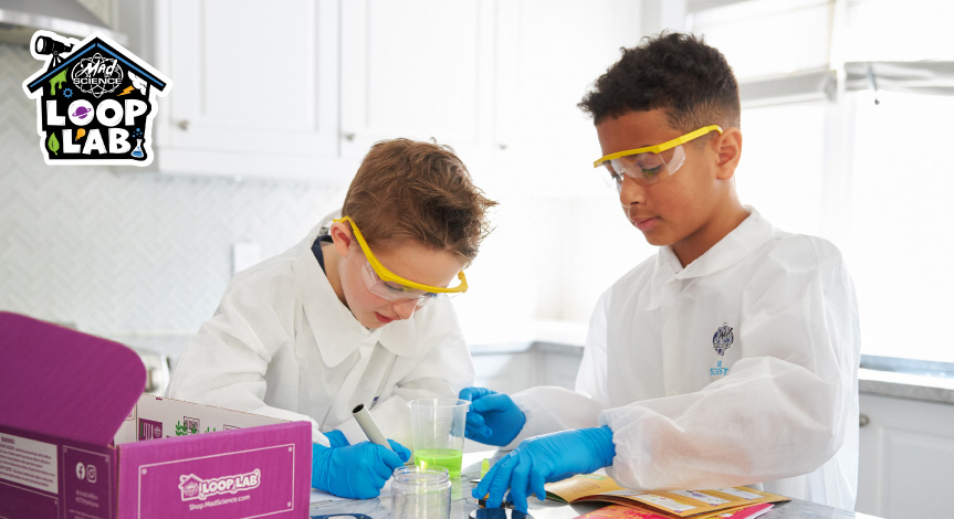 2 boys wearing mad science lab coats working on their mad science loop lab box competing one of the experiments 