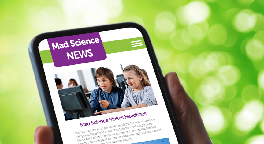 A woman looking at her phone. On the screen in the Mad Science website with the in the news page loaded.