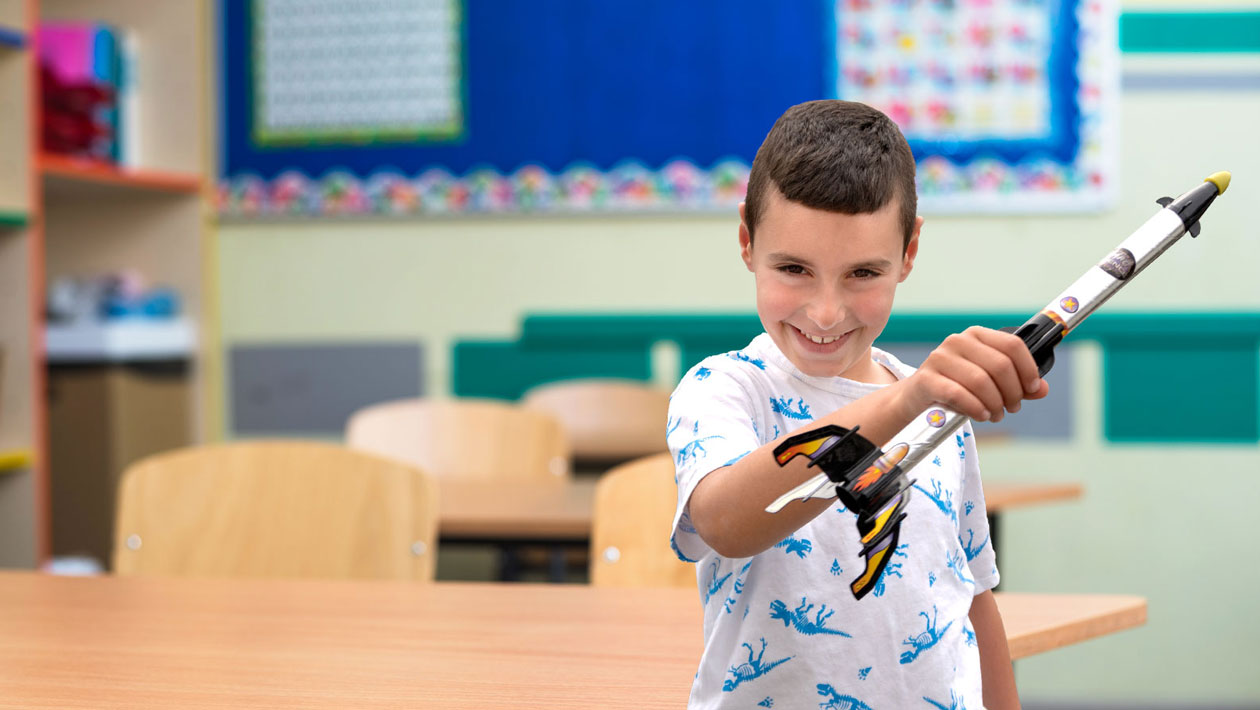 Boy smiling in a classroom while playing witha toy spaceship